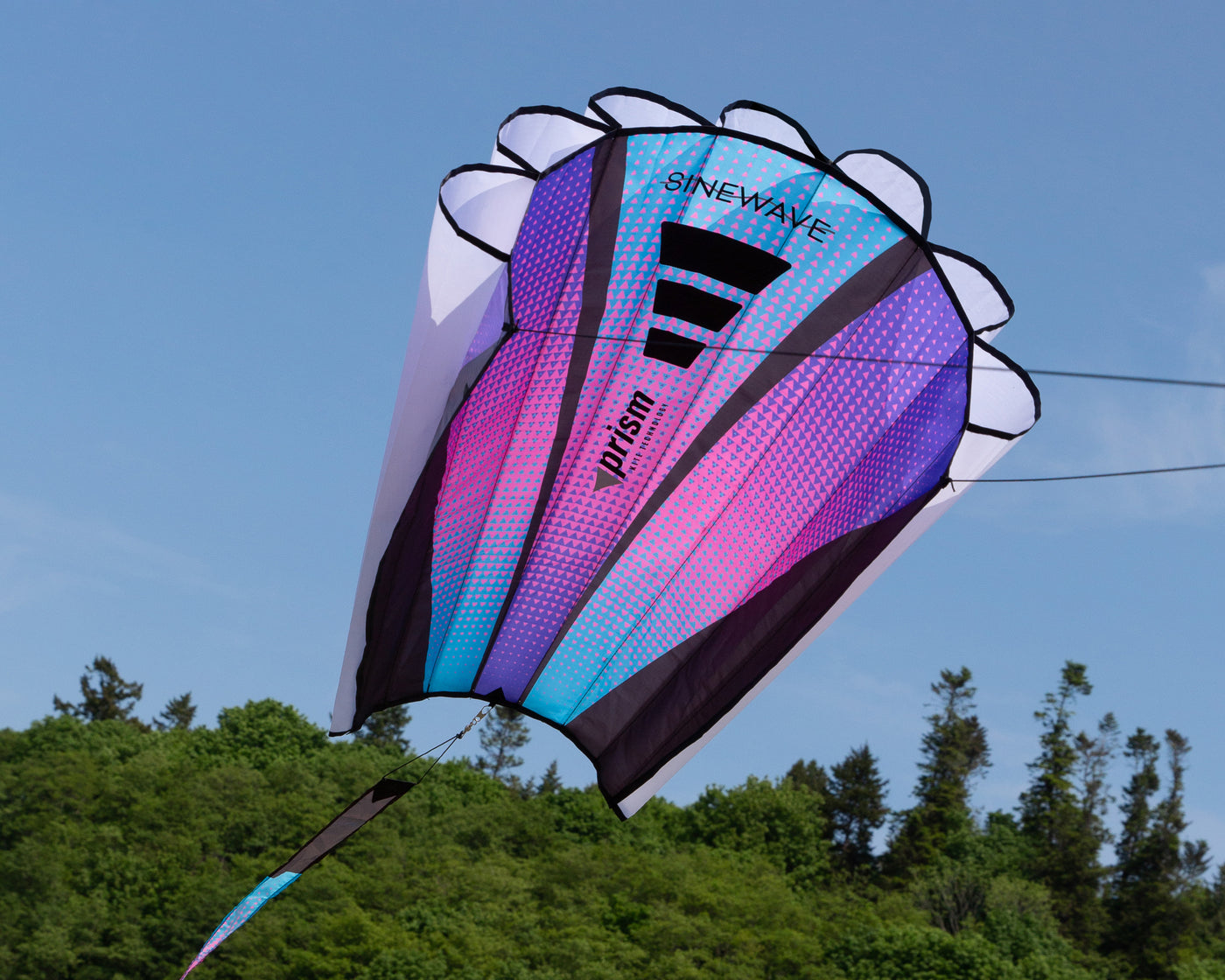The Ultraviolet Sinewave (blue, pink and purple) in flight with a blue sky and trees in the background.