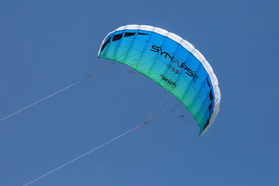 A blue/green Synapse 200 flying against a cloudless blue sky